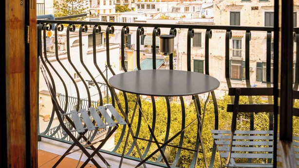 A balcony with a table and chairs, overlooking a hillside with buildings. - Residenza Ester (Amalfi)
