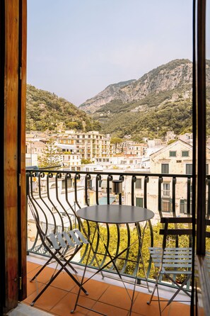 A balcony with a table and chairs, overlooking a hillside with buildings. - Residenza Ester (Amalfi)