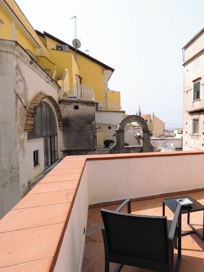 A rooftop terrace with a table and chairs, a stone archway, and a yellow building with a satellite dish. - Residenza Ester (Amalfi)
