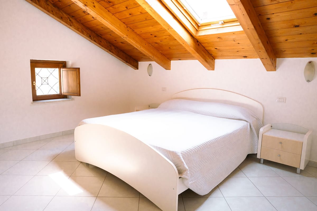 A bedroom with a bed, a nightstand, a window, and a skylight.