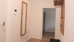Un pasillo con una puerta de madera, un espejo y un termostato en la pared.