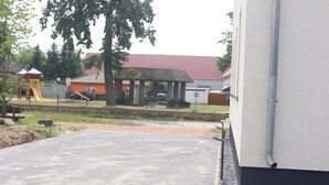 Un espacio exterior empedrado con un parque infantil, una zona de estar cubierta y un edificio con techo rojo.