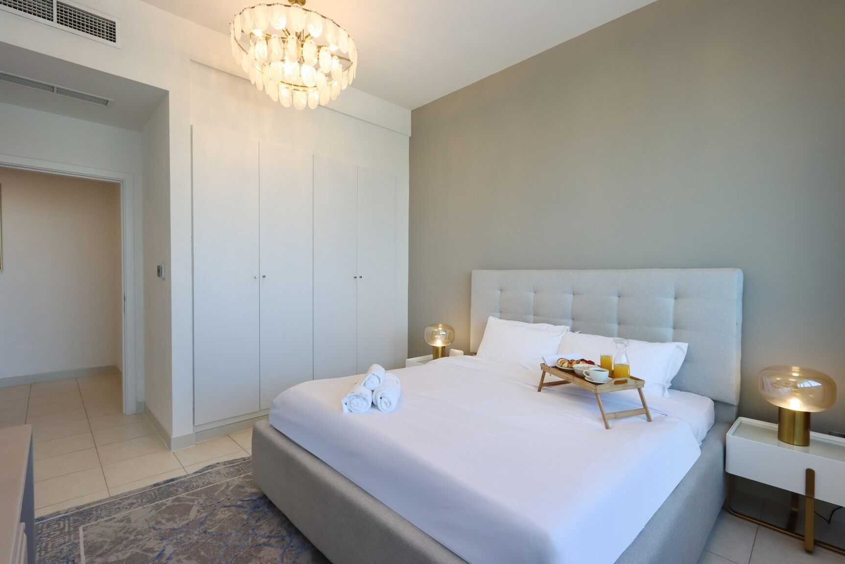 Quarto moderno com cama grande, cômoda, lustre e mesa de cabeceira com abajur.
