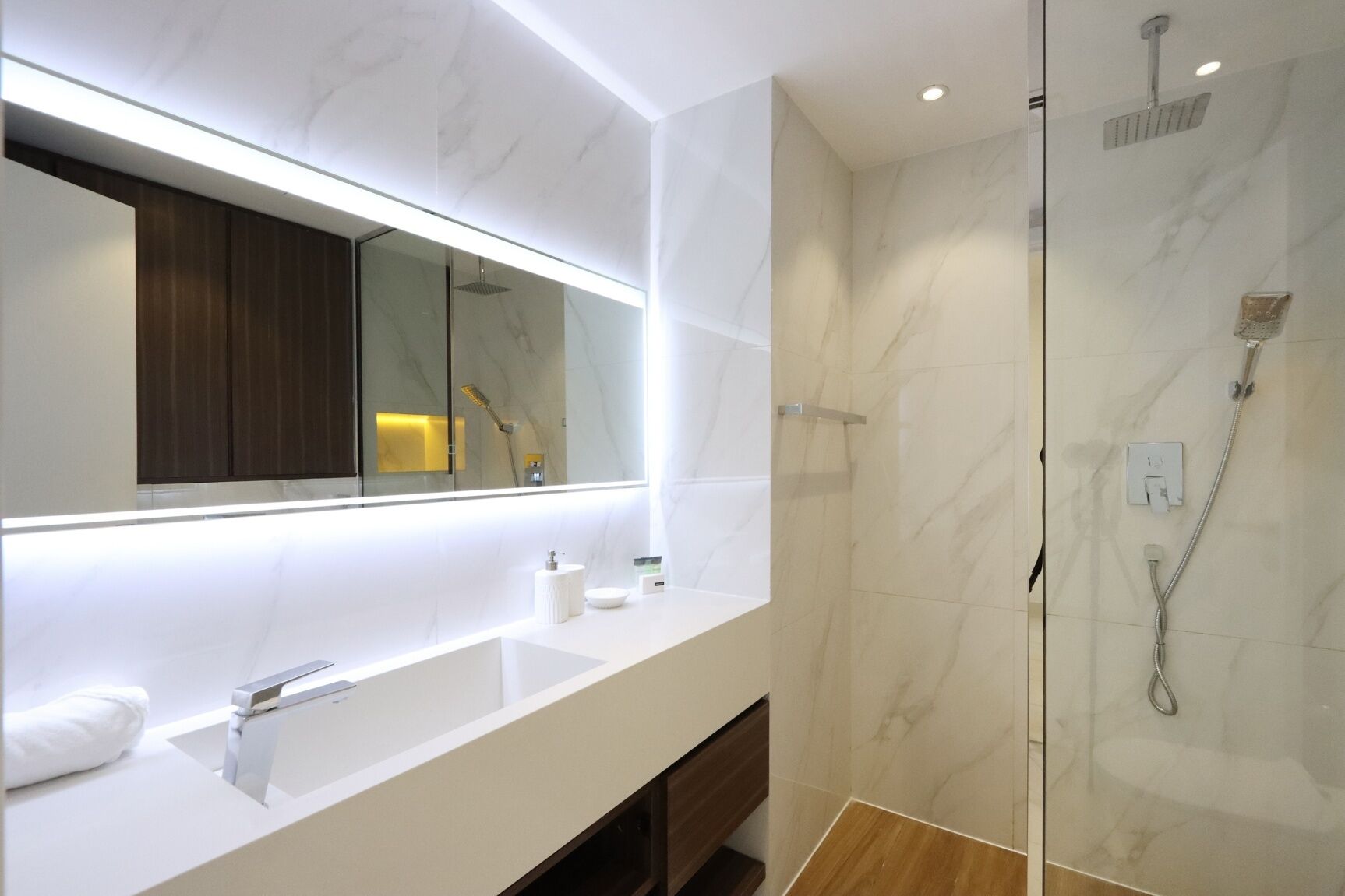 A modern bathroom with a large mirror, a white sink, a glass-enclosed shower, and a wooden vanity.