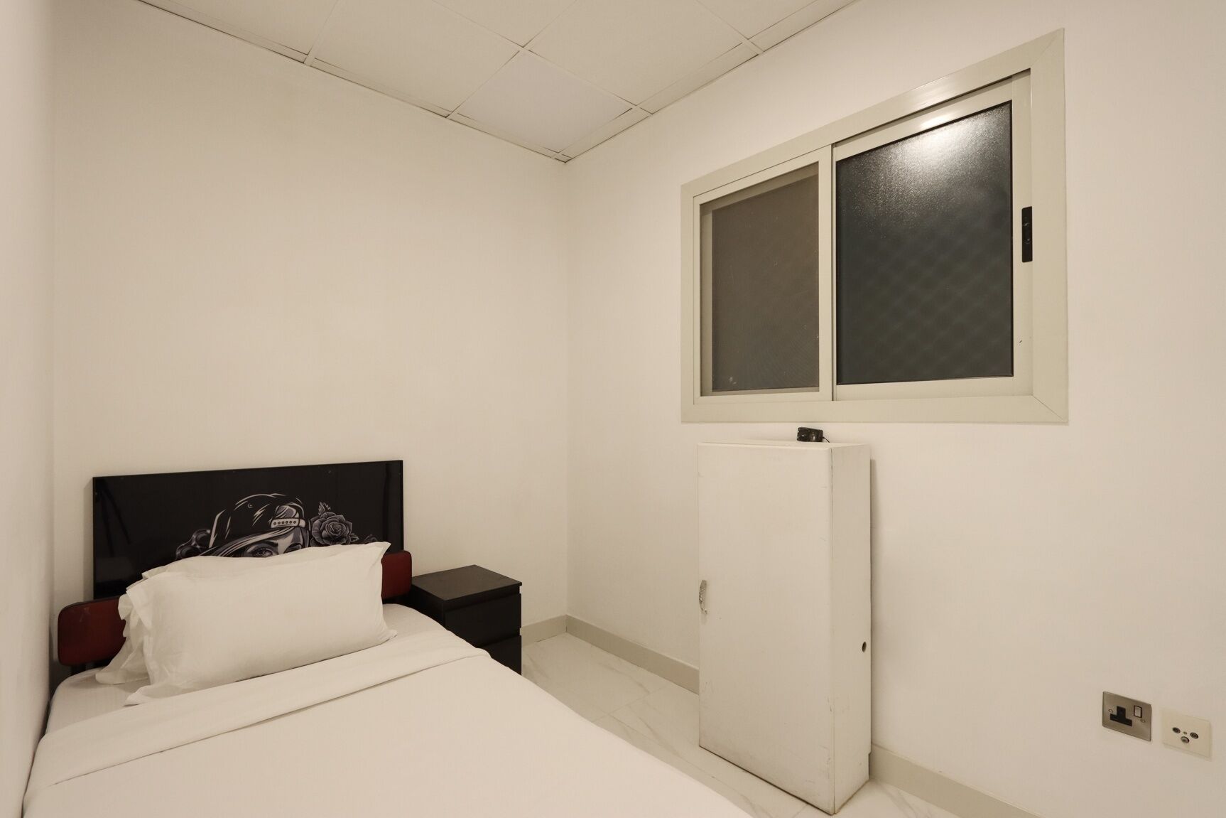 Een slaapkamer met een bed, nachtkastje, kledingkast en een raam.