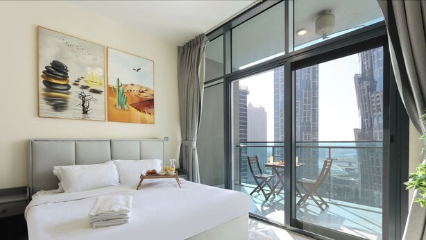 Et moderne hotelværelse med en stor seng, en balkon med bord og stole, samt udsigt over byen.