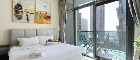A modern hotel room with a large bed, a balcony with a table and chairs, and city views.