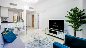 Een moderne woonkamer met een flatscreen televisie, een glazen salontafel, een bank en een eethoek met stoelen.