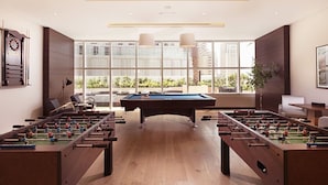 Een moderne, overdekte recreatieruimte met twee tafelvoetbaltafels, een pooltafel en grote ramen met uitzicht op de stad.