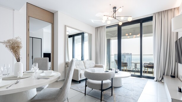A modern, well-lit living room with a dining area, a sofa, and a balcony with a view.