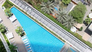 A rectangular swimming pool with a surrounding walkway, palm trees, and lounge chairs.
