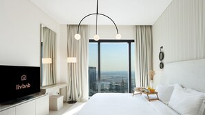 A modern hotel room with a large bed, a TV displaying the Livbnb logo, a city view, and a breakfast tray on the nightstand.