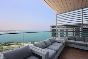 A balcony with wicker furniture and a view of the sea and city skyline.