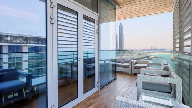 Ein Balkon mit Glastüren, Korbmöbeln und Blick auf eine Stadtlandschaft und Wasser.