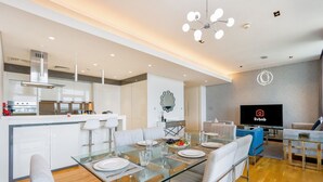 Una sala de estar moderna con una mesa de comedor de vidrio, sofás blancos y un televisor de pantalla plana.