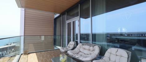 A balcony with glass railings, cushioned chairs, a glass table, and a view of the sea.