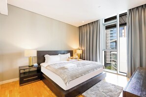 Une chambre d’hôtel moderne avec un grand lit, des tables de chevet, une vue sur un immeuble par la fenêtre et un balcon.