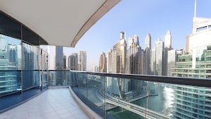 Uma varanda com guarda-corpo de vidro, com vista para um horizonte urbano repleto de edifícios modernos e um rio.