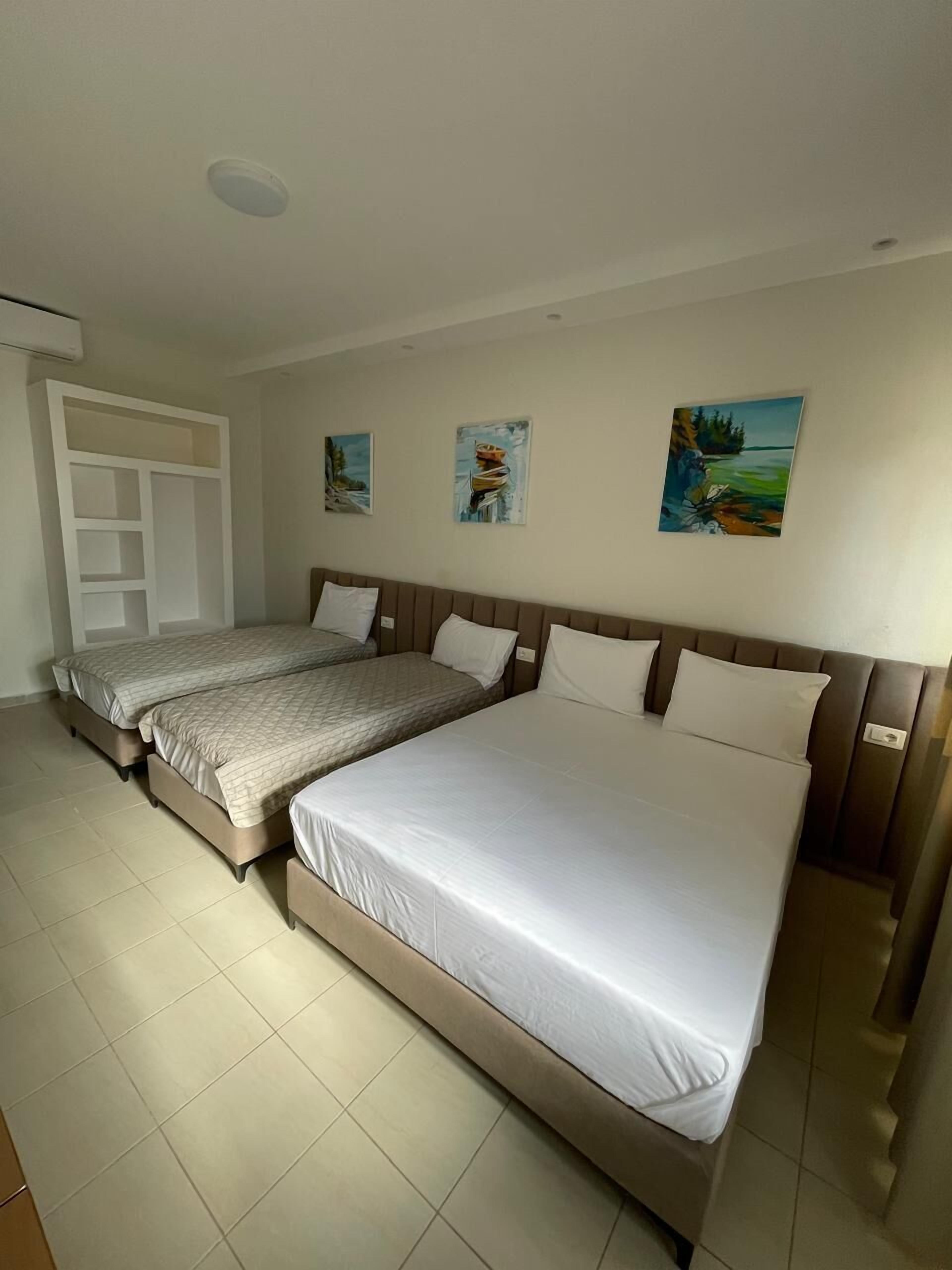 Habitación de hotel con dos camas, un armario y tres cuadros en la pared.