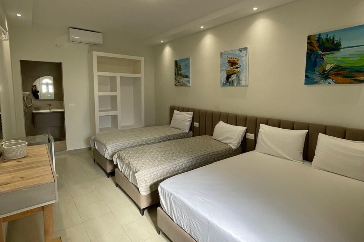 Ein Hotelzimmer mit zwei Betten, einem Schreibtisch, einem Stuhl, einem Spiegel und einer kleinen Küchenzeile.