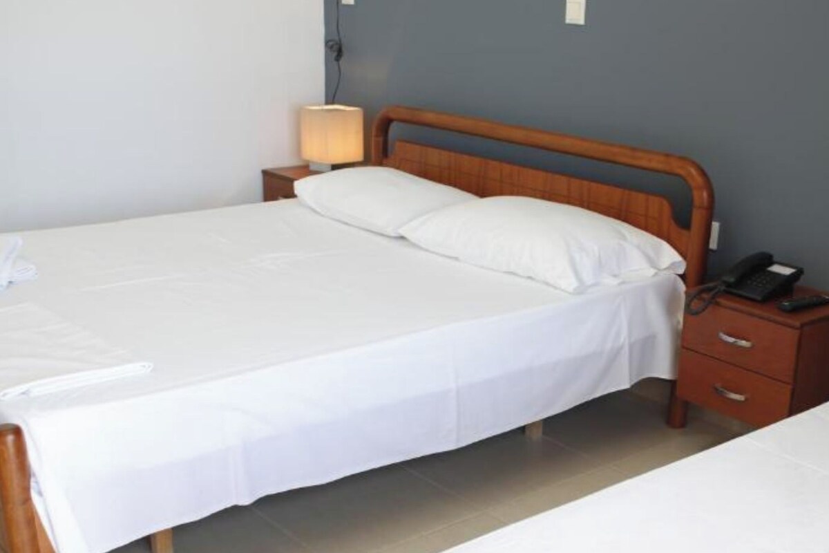Ein Doppelbett mit Holz-Kopfteil, ein Nachttisch mit Lampe und ein Telefon.