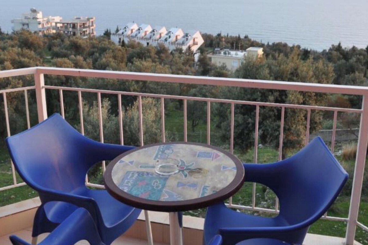 Ein Balkon mit zwei blauen Plastikstühlen und einem kleinen runden Tisch mit Glasplatte.
