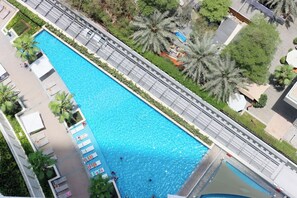 Eine Vogelperspektive auf einen rechteckigen Pool mit einer umlaufenden Promenade, Palmen und einem Gebäude mit flachem Dach.