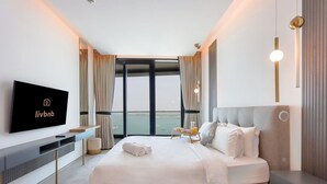 A modern hotel room with a large bed, a flat-screen TV, a bedside table, and a view of the sea.