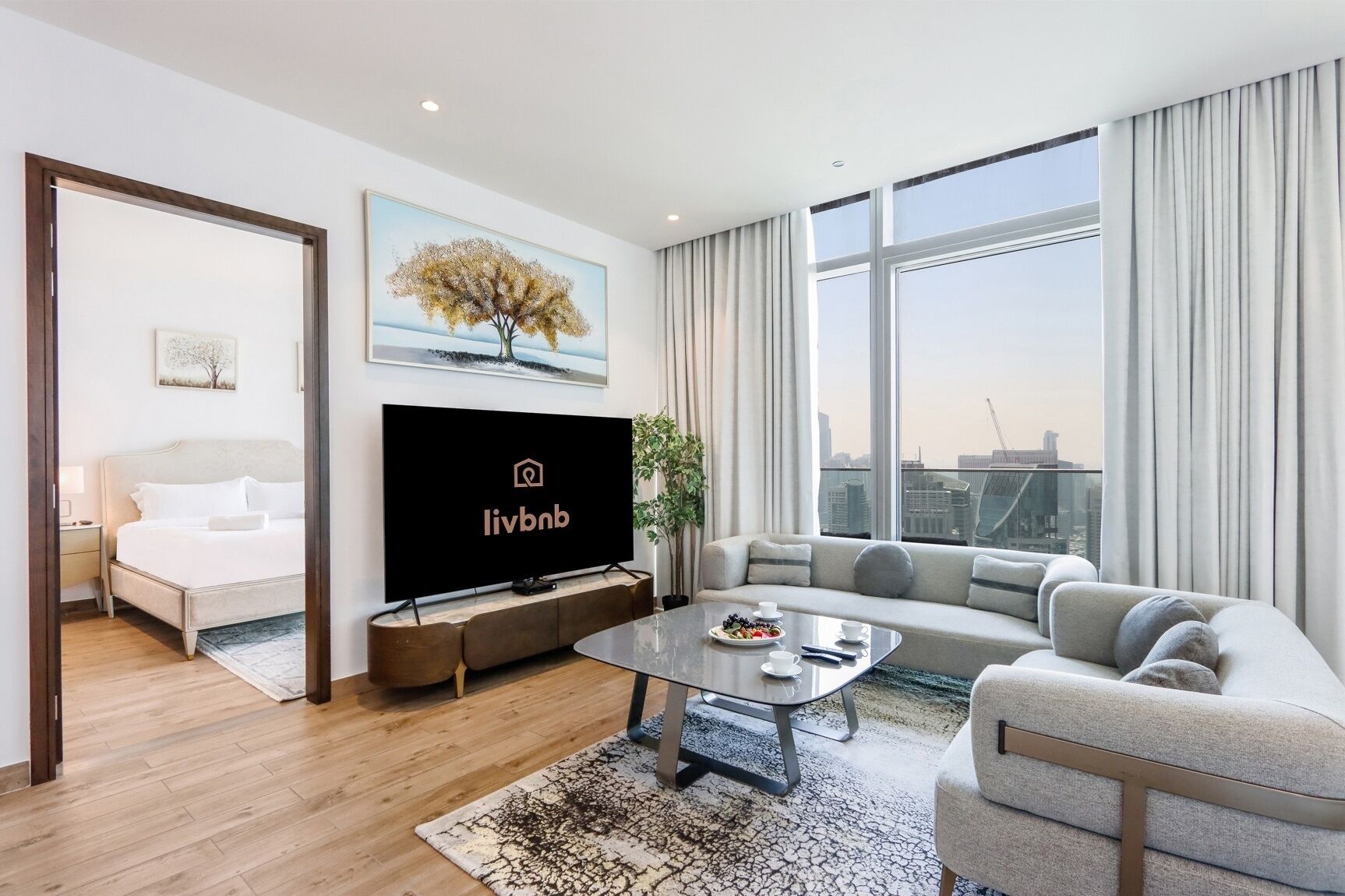 Ein modernes Hotelzimmer mit Bett, Fernseher, Sofa, Couchtisch und einem großen Fenster mit Blick auf die Stadt.