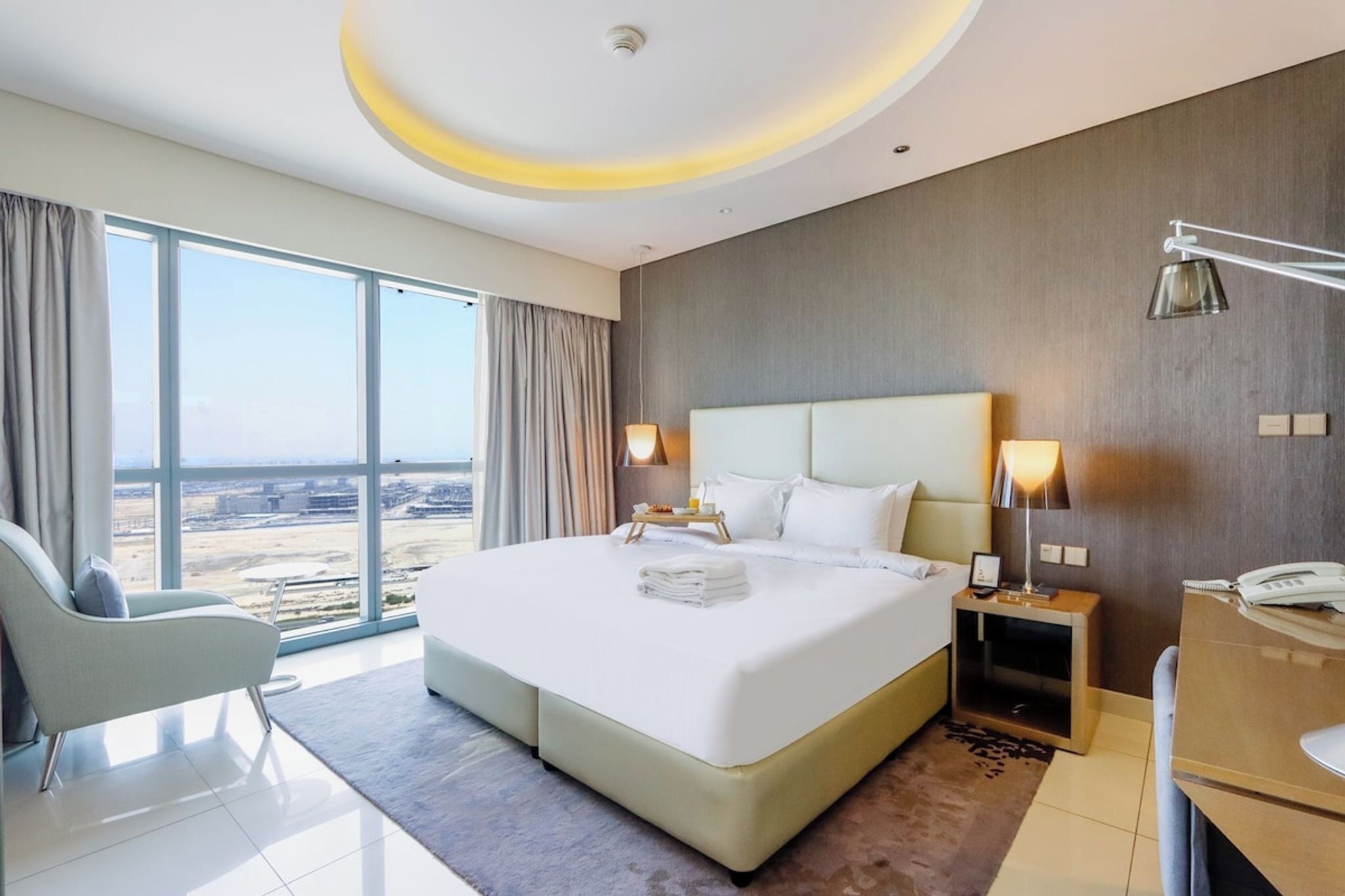 Ein Hotelzimmer mit einem großen Bett, Nachttischlampen, einem Schreibtisch und Blick auf die Stadt.