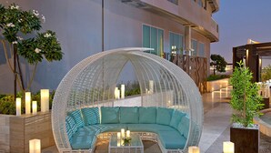A white wicker outdoor seating area with teal cushions and a glass table, surrounded by candles and plants.