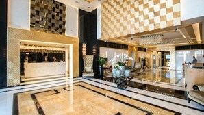 A spacious lobby with a reception desk, seating area, and a checkered ceiling pattern.