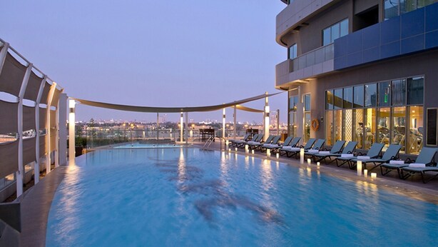 A rooftop pool with lounge chairs, a city view, and a modern building structure.