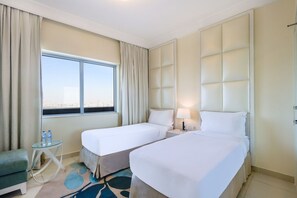 Une chambre d’hôtel avec deux lits, une petite table avec des bouteilles d’eau, une lampe et une vue sur la ville par la fenêtre.