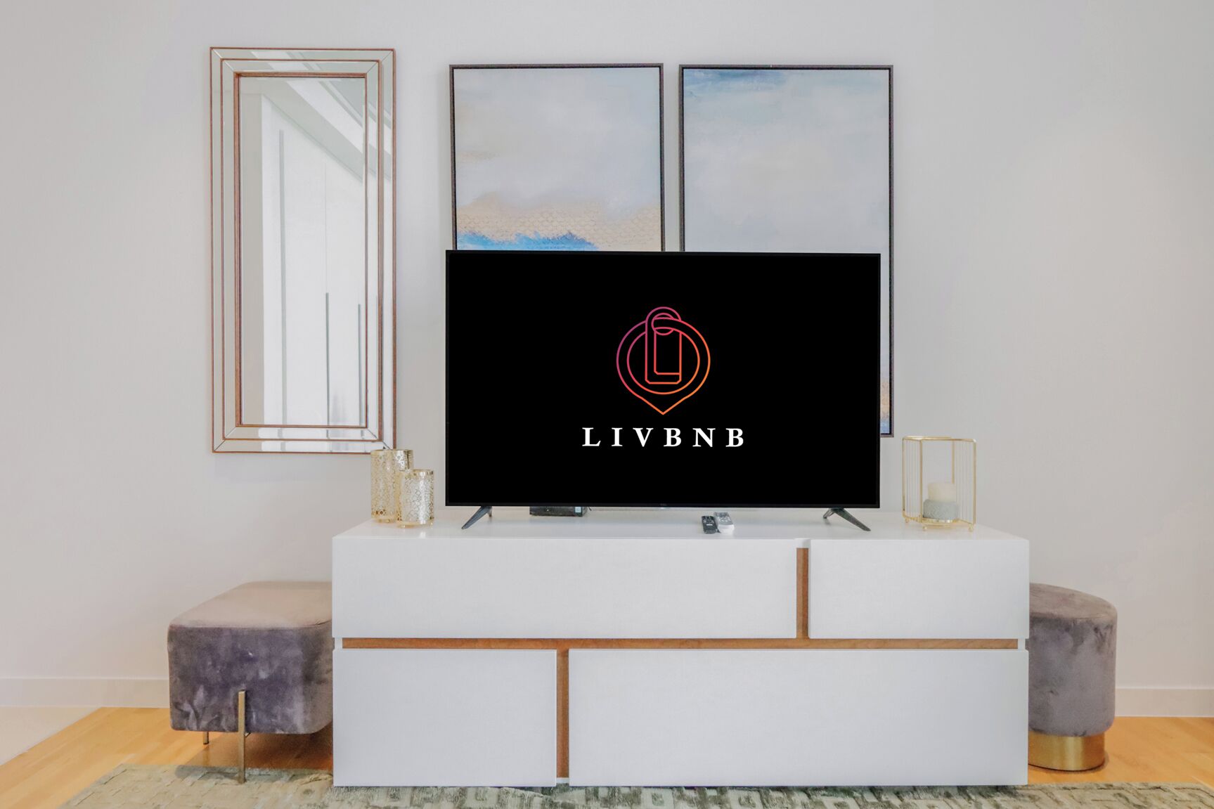 A modern living room with a flat-screen TV on a white console, framed artwork above, and a mirror on the wall.