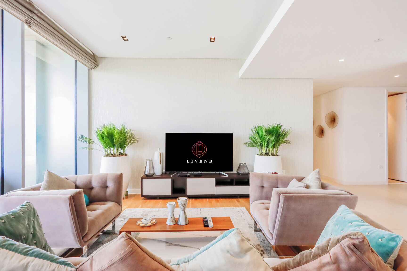 A modern living room with a flat-screen TV, two potted plants, and a sofa set.