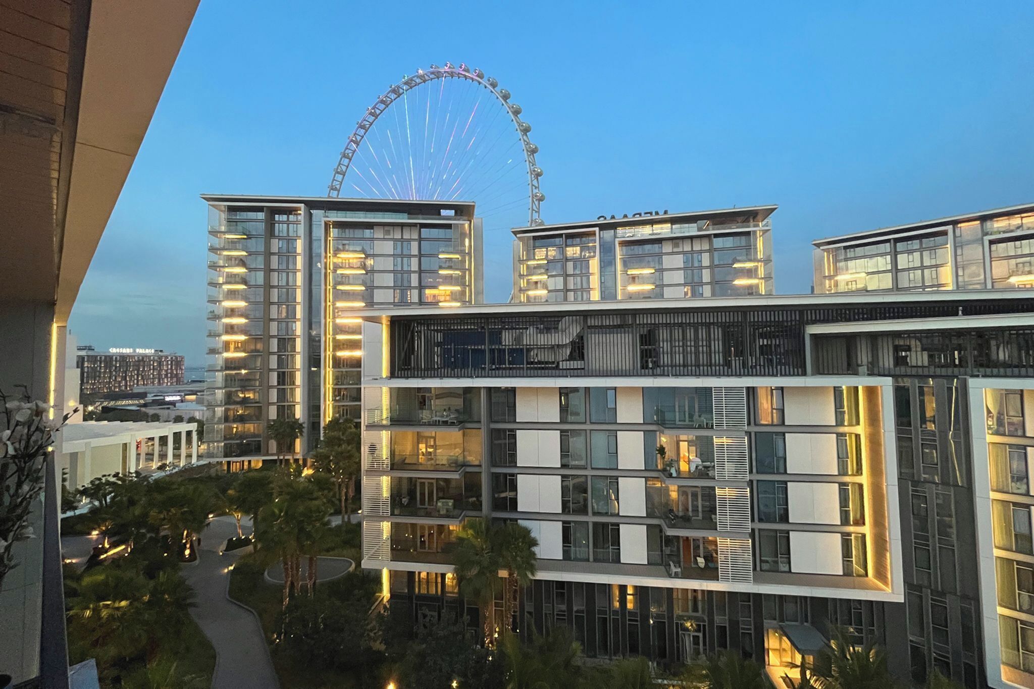 A modern hotel with multiple floors, large windows, and a view of a Ferris wheel in the background.
