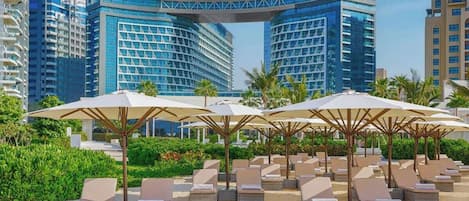 A modern hotel with a curved glass facade, outdoor lounge chairs, and umbrellas.