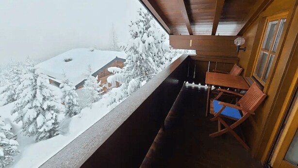 En stuga av trä med en balkong som vetter ut mot ett snötäckt landskap.