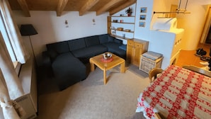 Ett mysigt vardagsrum med en soffa, ett litet bord och ett rött och vitt rutigt bordsduksöverdrag. I hörnet står ett träskåp och en tvättkorg.