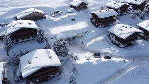 En snötäckt stuga med flera trähus, en skidlift och parkerade bilar.