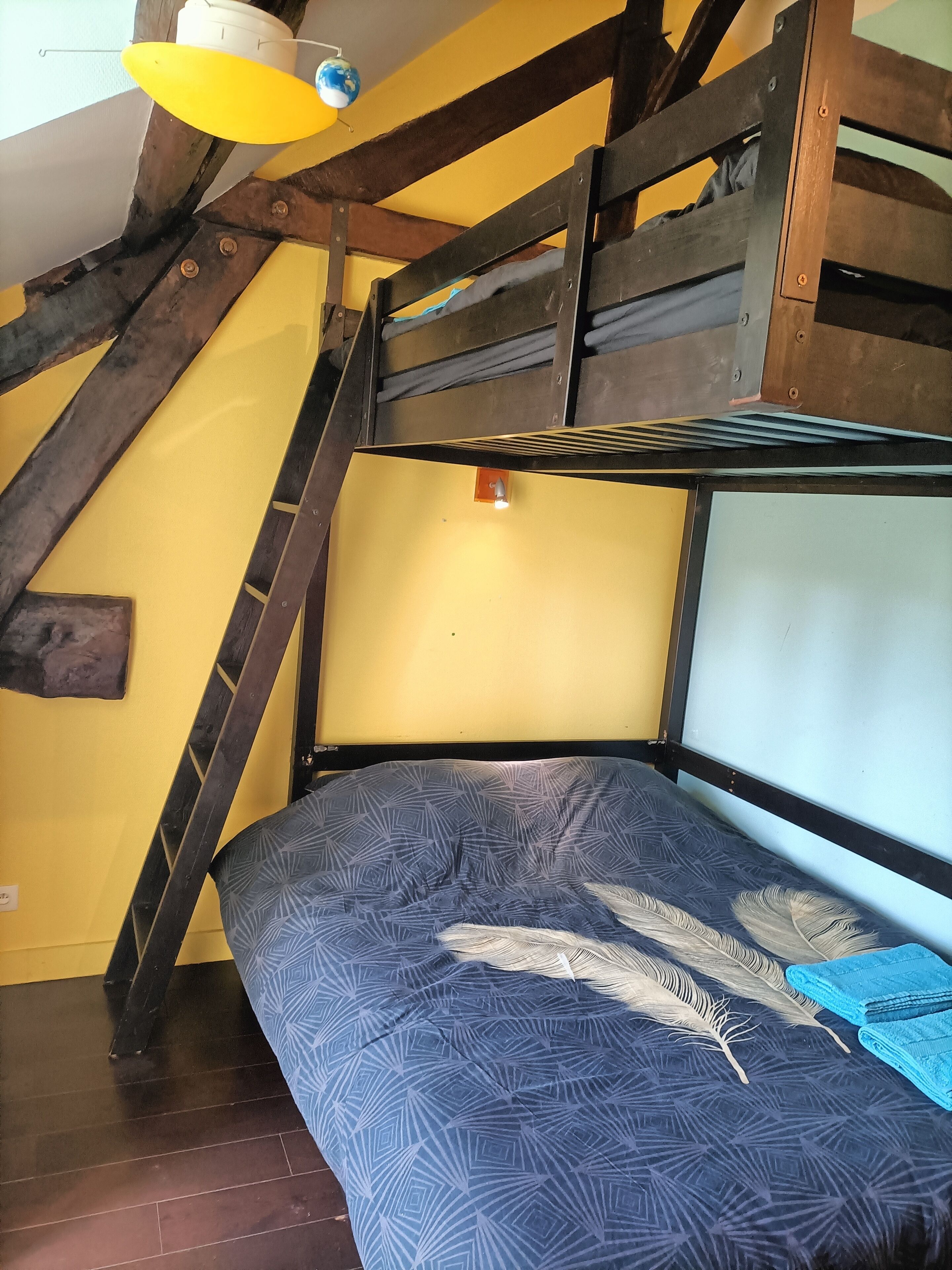 A bunk bed with a patterned bedspread, wooden beams, and a globe hanging from the ceiling.