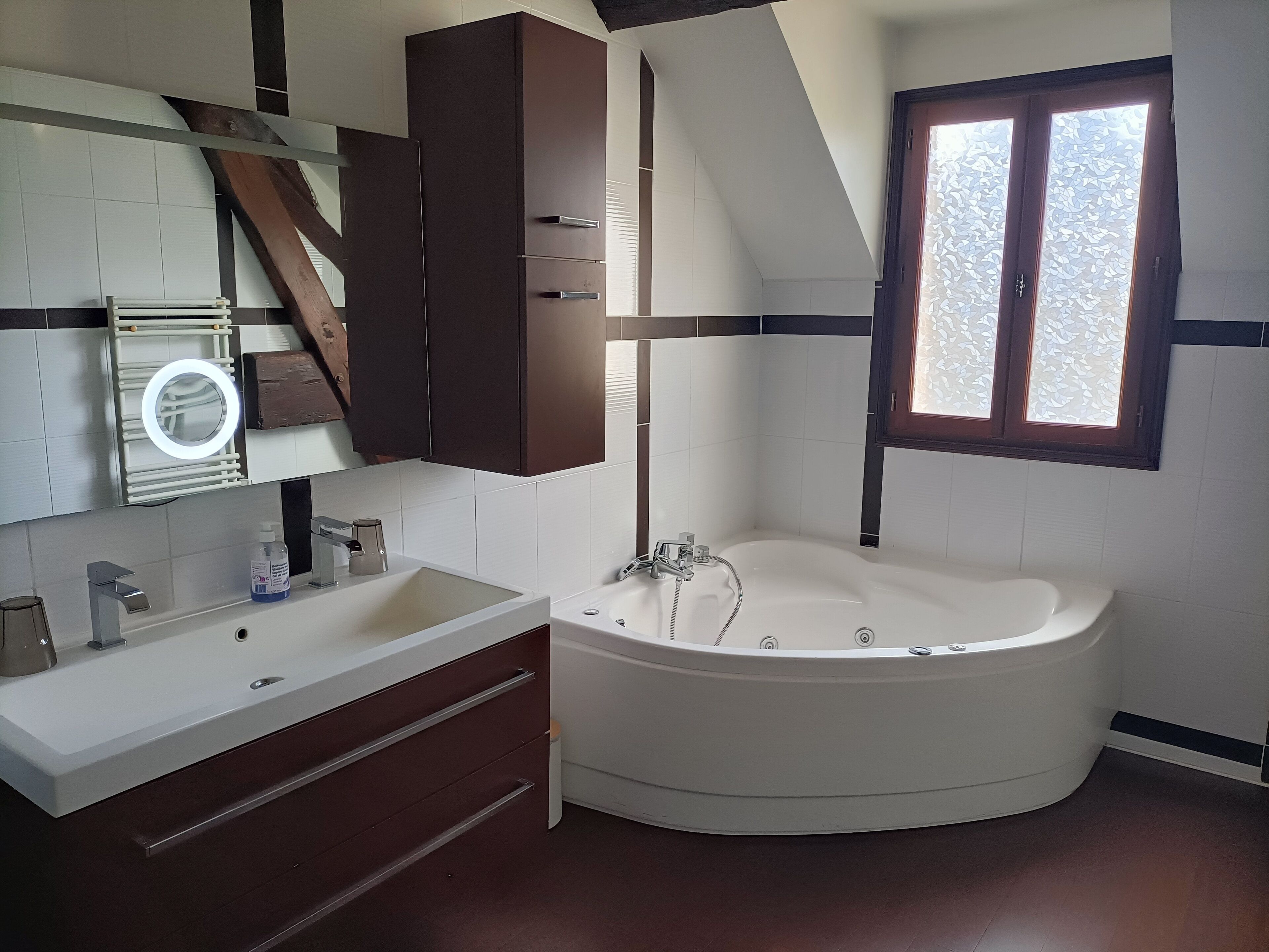 Ein modernes Badezimmer mit einer freistehenden Badewanne, einem Waschtisch mit Spiegel und einem Fenster mit Milchglas.