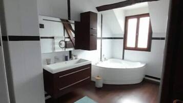 Un bagno con una vasca da bagno bianca, un lavandino e uno specchio. Una finestra permette l'ingresso di luce naturale.