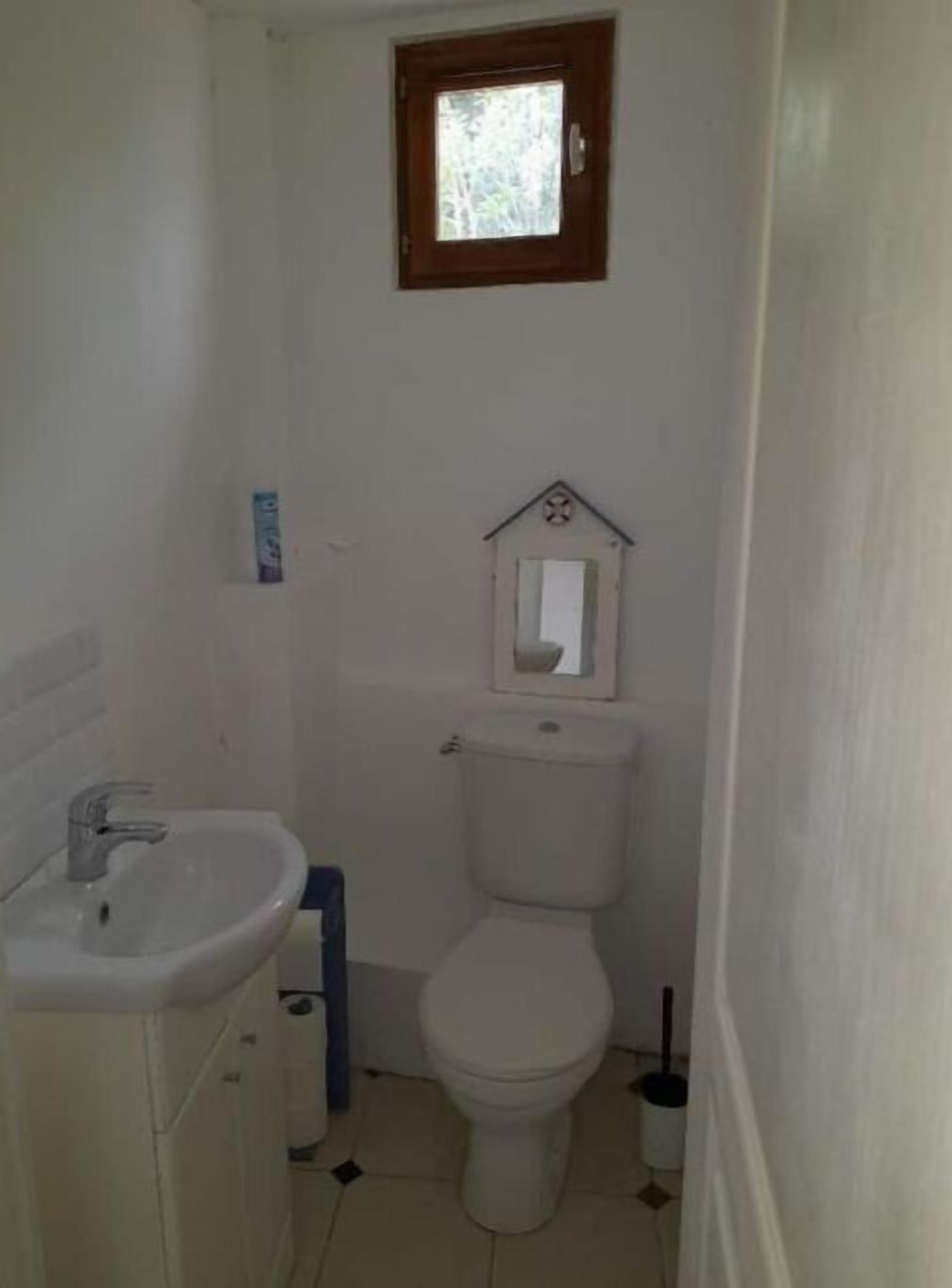 Ein kleines, schlichtes Badezimmer mit Waschbecken, Toilette und einem kleinen Fenster über der Toilette.