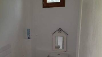 Ein kleines, schlichtes Badezimmer mit Waschbecken, Toilette und einem kleinen Fenster über der Toilette.