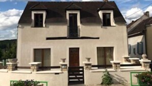 Une maison à deux étages, dotée d’une façade symétrique, d’une entrée centrale et d’un petit porche agrémenté de plantes en pot.