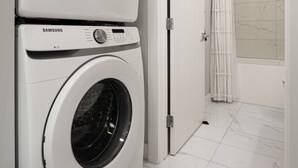 Un lavadero con dos lavadoras apiladas, un baño con ducha y suelo de baldosas.