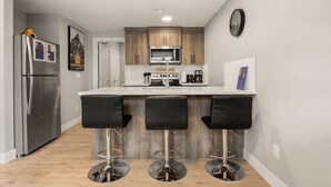 Una cocina moderna con una isla central, taburetes de bar, un refrigerador y un microondas.
