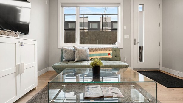 Una sala de estar moderna con una mesa de centro de vidrio, un sofá con cojines, un televisor sobre un mueble bajo y vistas a través de un ventanal.